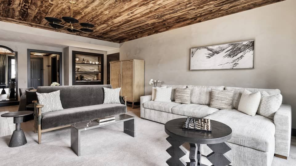 Renovated Four Seasons Vail suite lounge with contemporary sofas, wood ceiling, and built-in shelving
